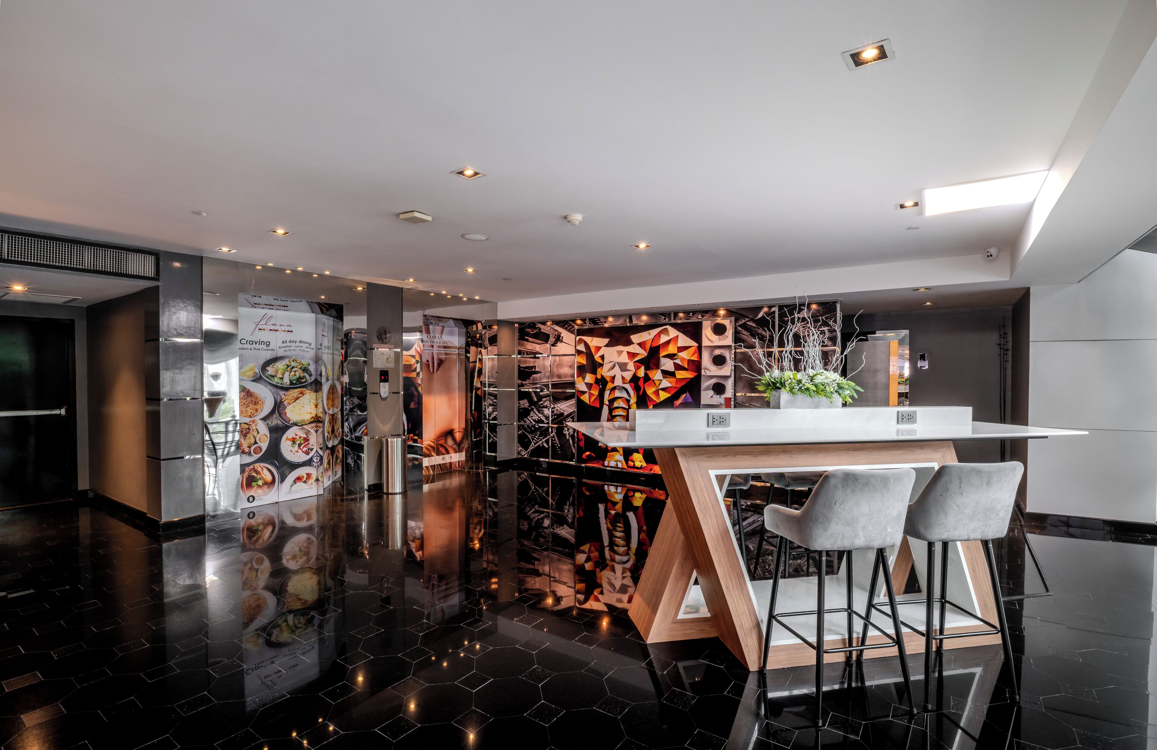 A modern bar area with a reflective black floor, a white bar counter, and two grey bar stools.