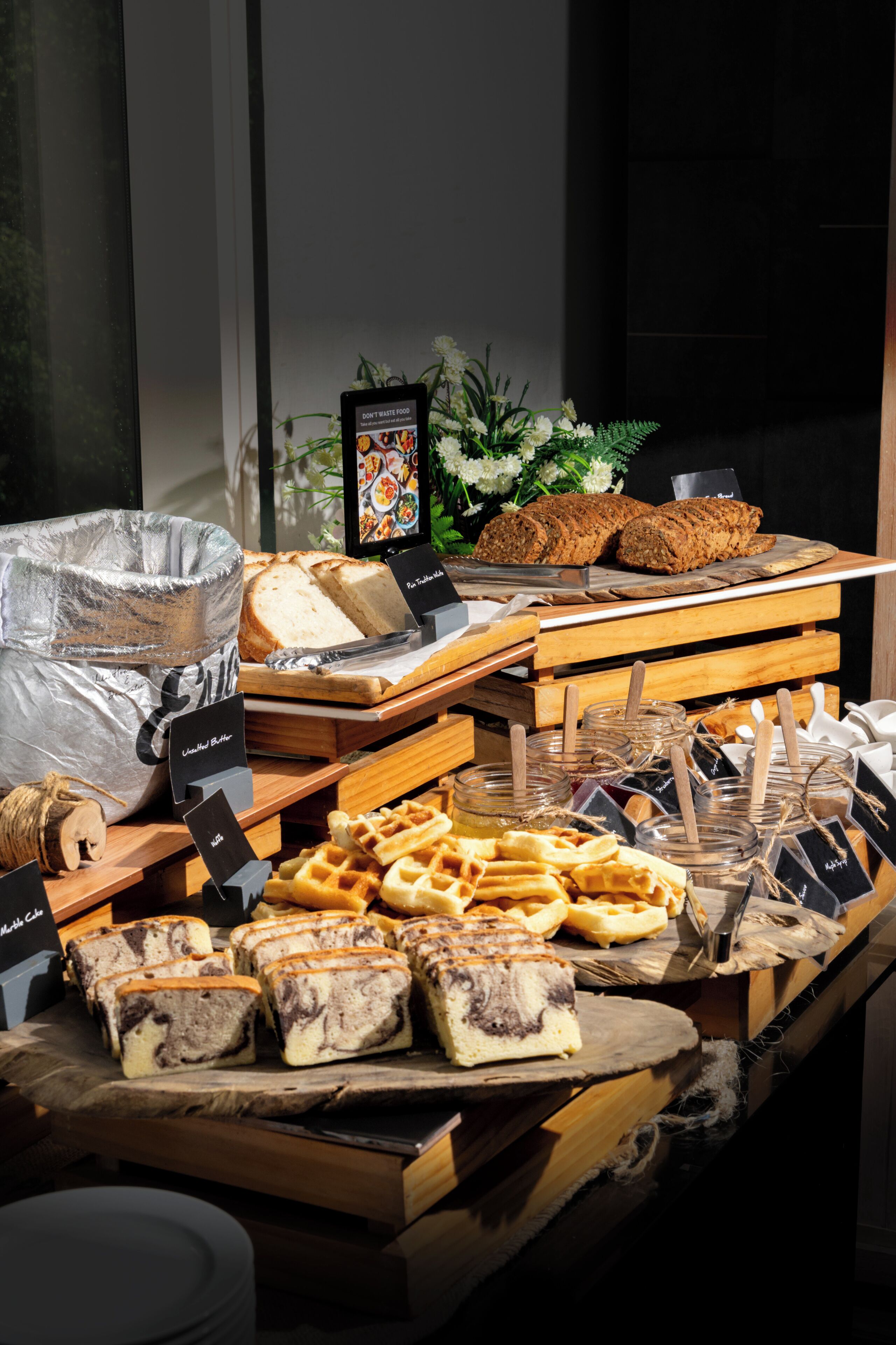 A buffet table with various food items including bread, waffles, and pastries.