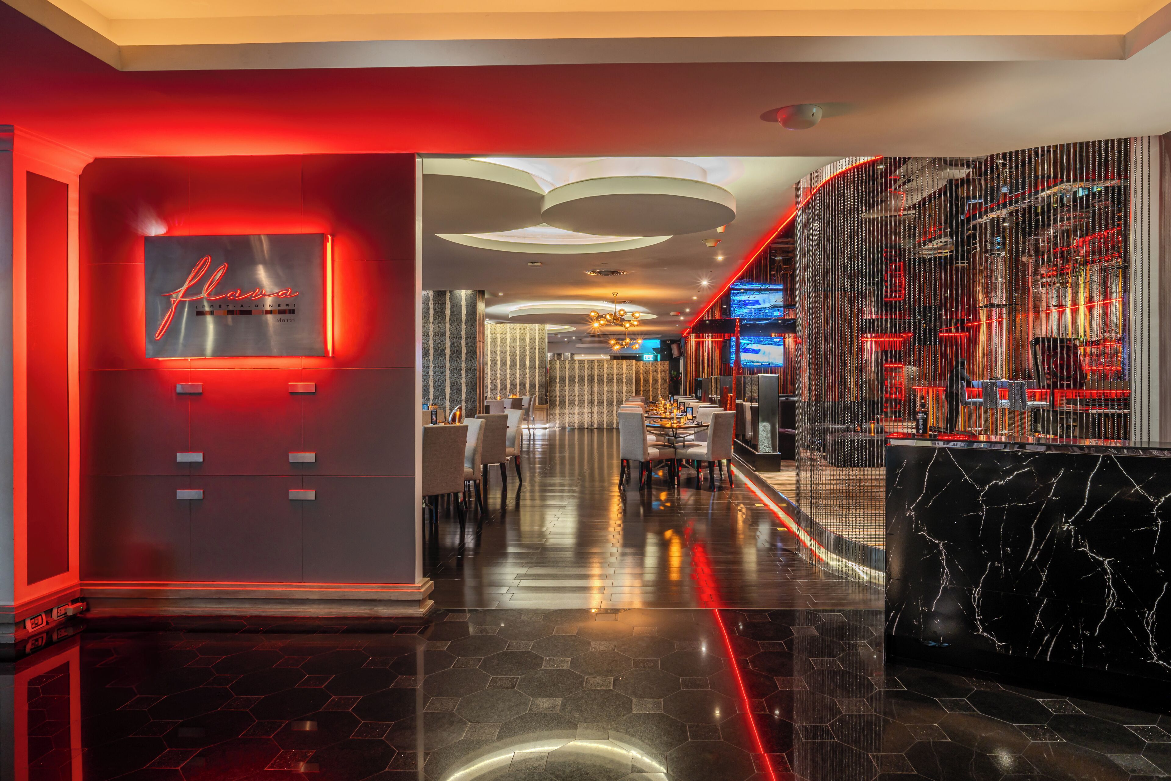 A modern hotel lobby with a red neon sign, a bar area, and a seating area with a reflective floor.