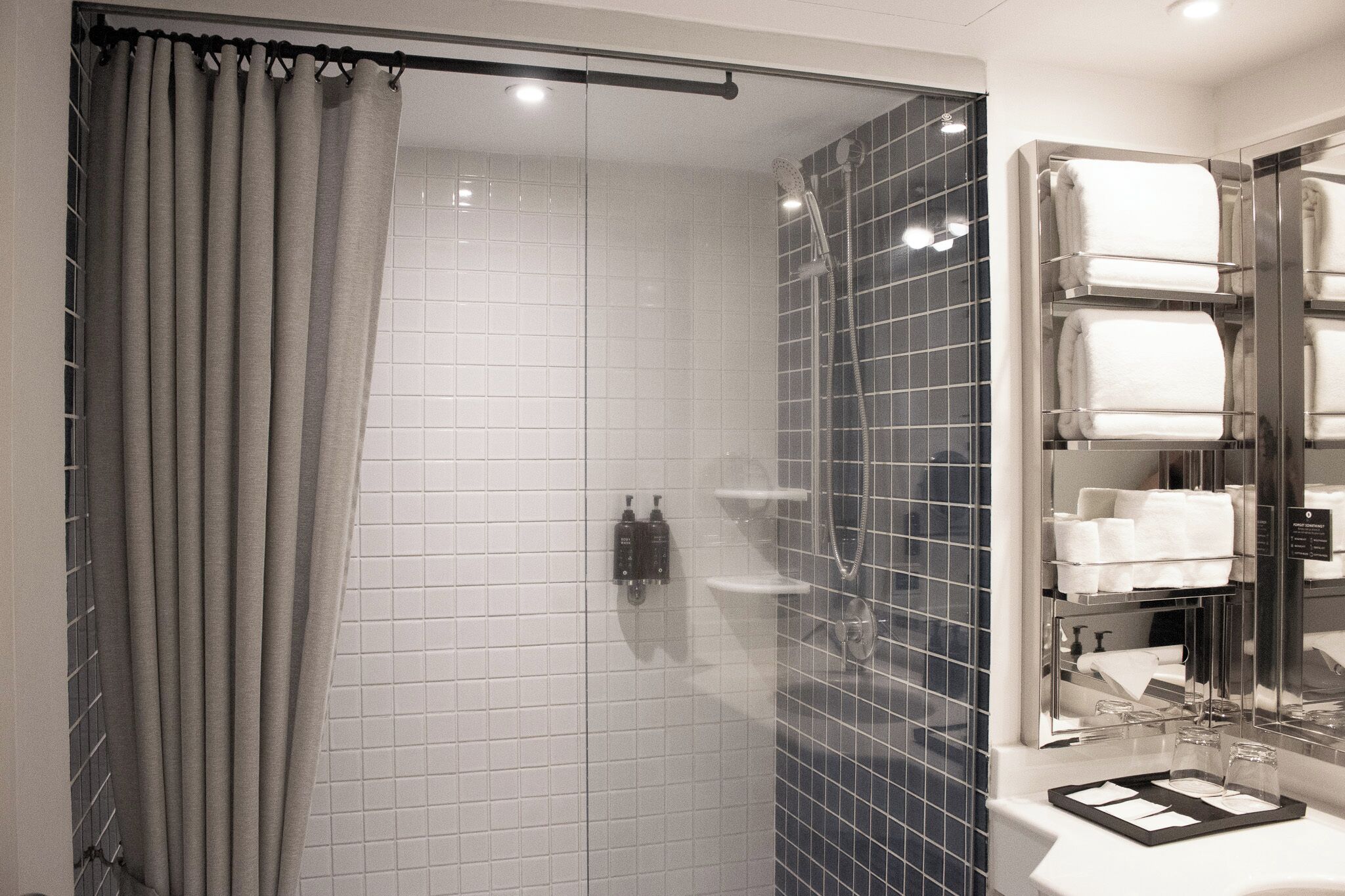 A modern bathroom with a glass shower enclosure, white tiled walls, and a built-in towel rack.