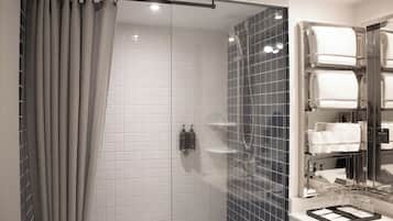 A modern bathroom with a glass shower enclosure, white tiled walls, and a built-in towel rack.