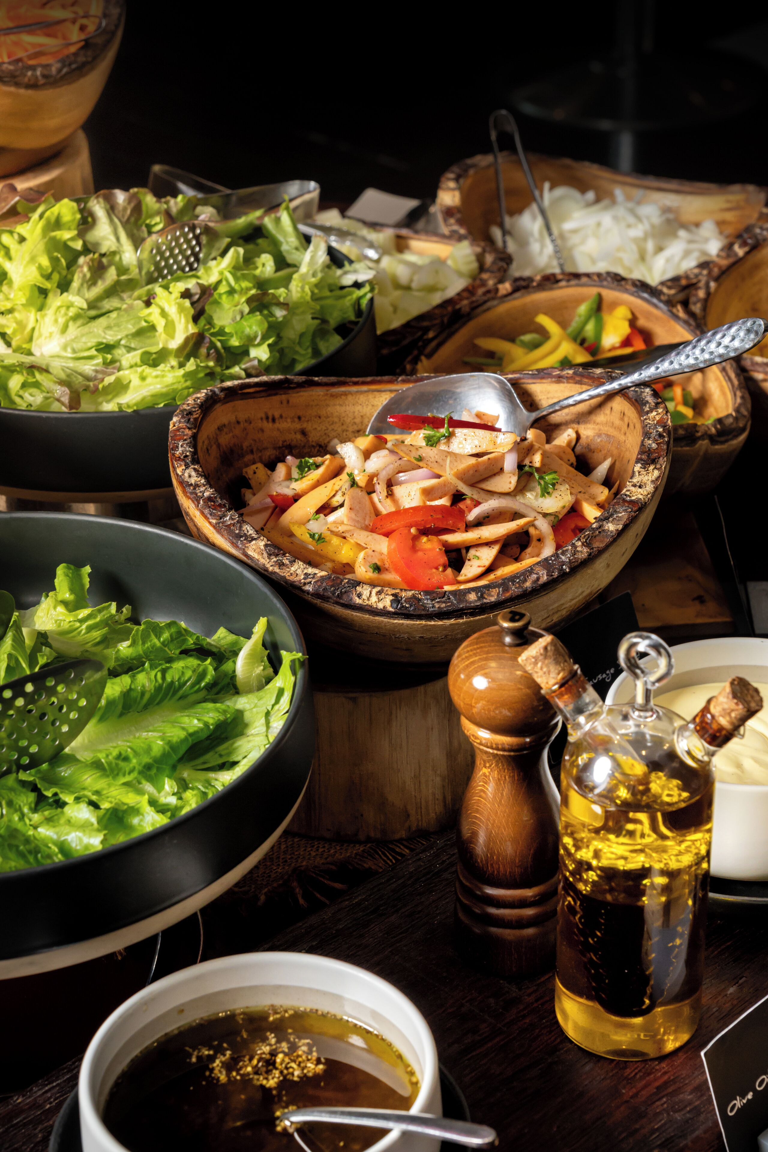 A wooden table with various dishes, including a bowl of salad, a bowl of rice, and a bottle of olive oil.