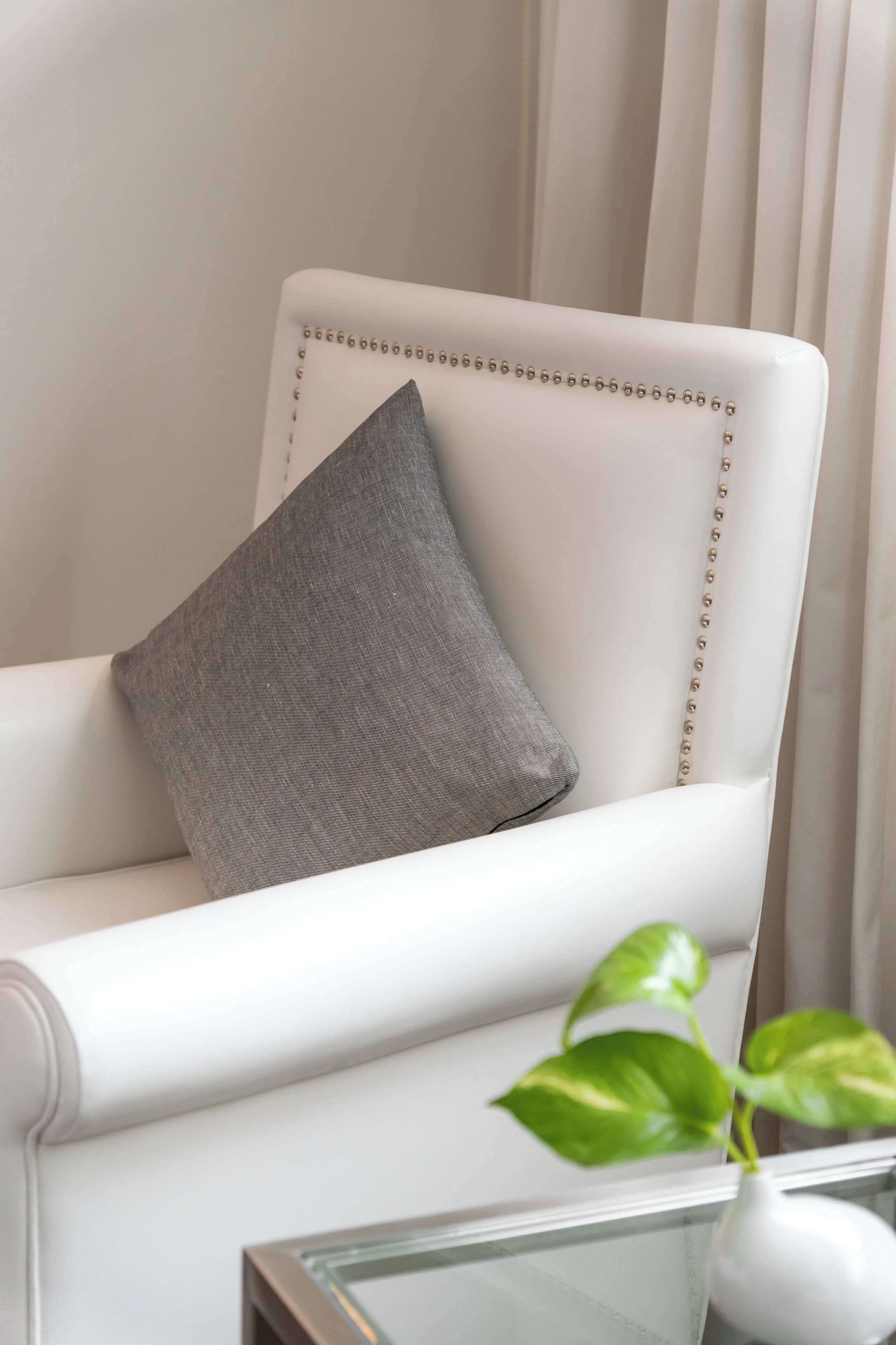 A white armchair with a gray pillow and a glass vase with a plant.