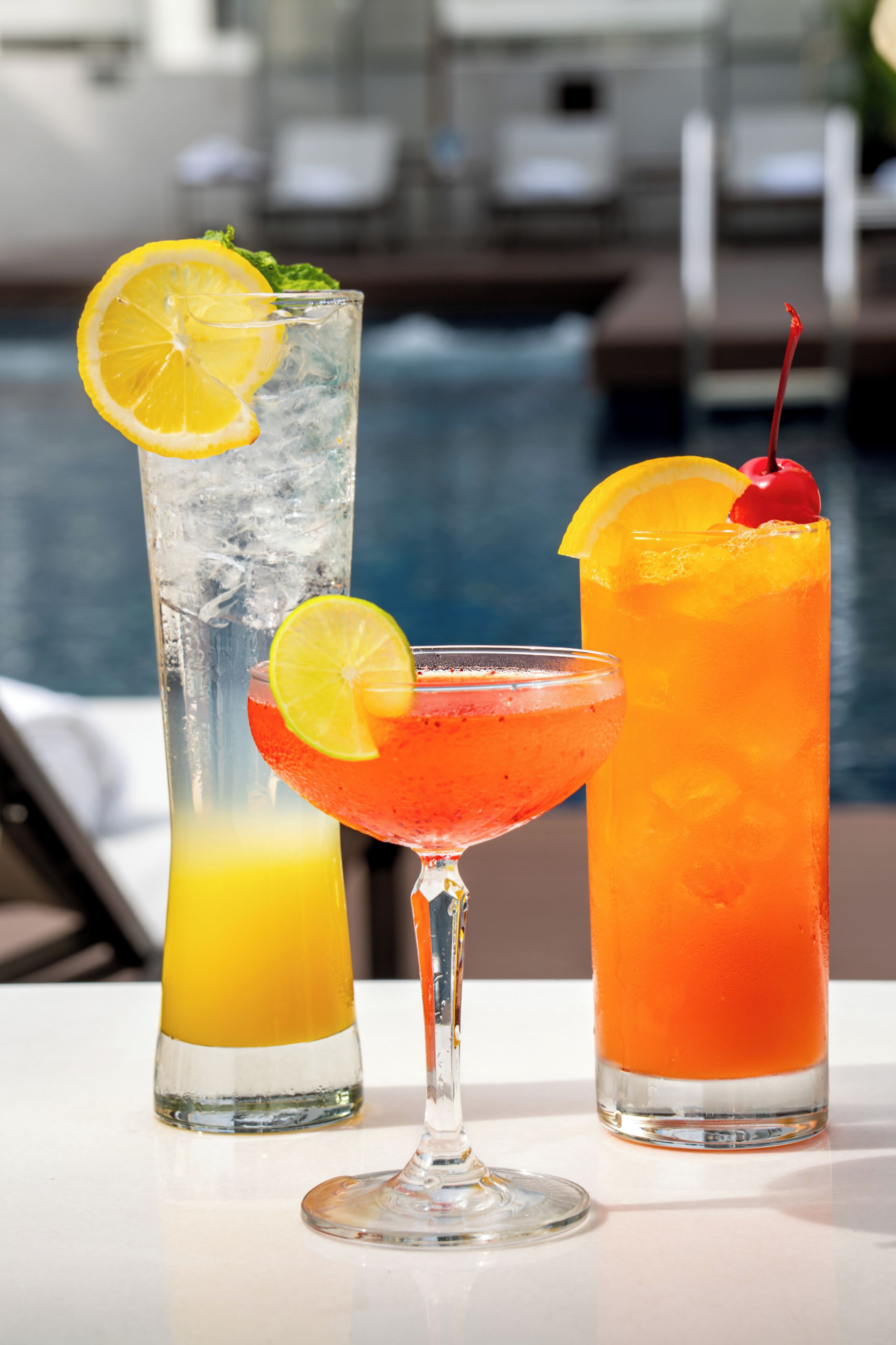 Trois cocktails sont posés sur une table, avec une piscine en arrière-plan.