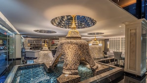 Un lobby lujoso con una fuente central, candelabros modernos y decoración de pared con diseños.