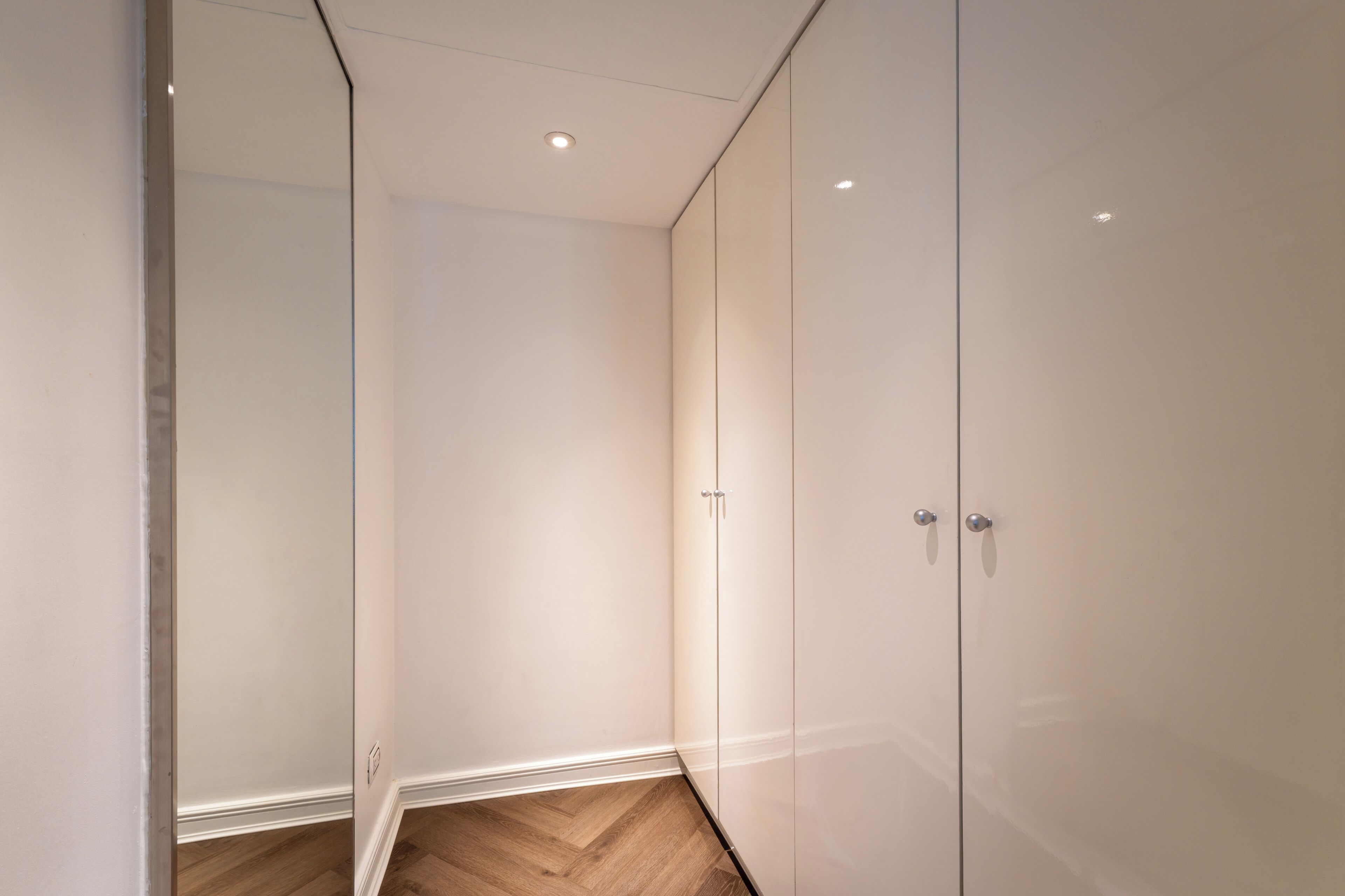 A modern room with a wooden herringbone floor, white walls, and a large wardrobe with two doors.