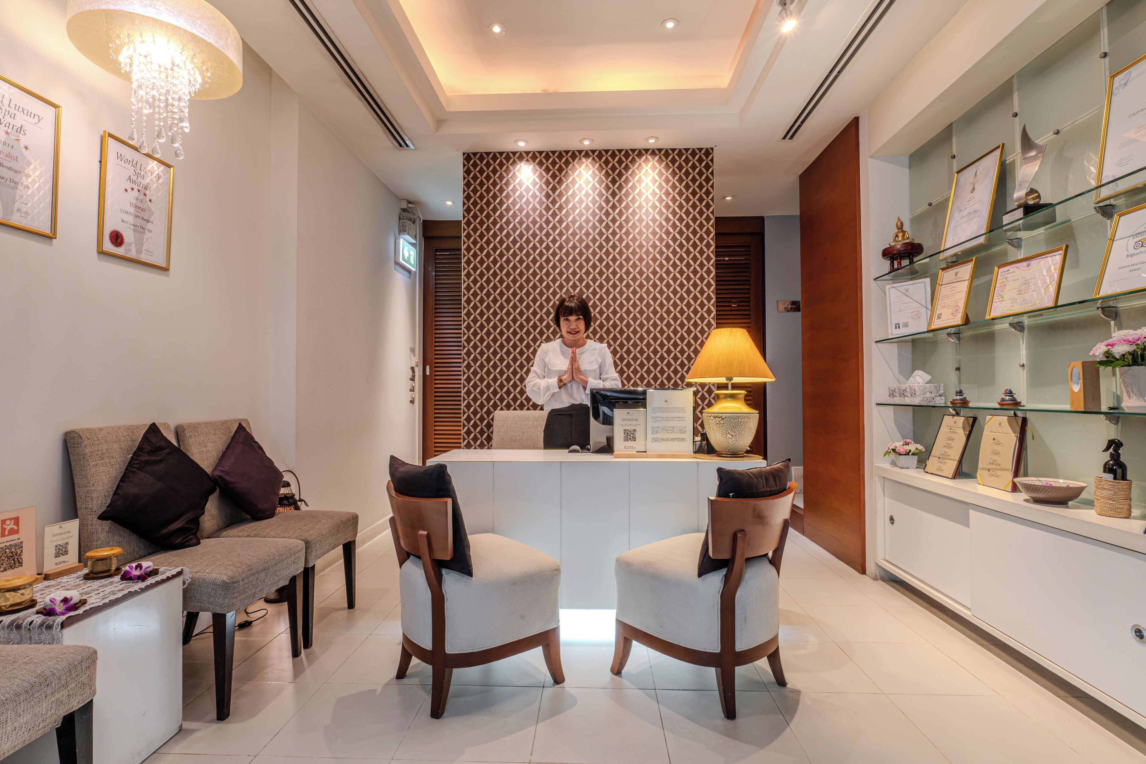A reception area with a reception desk, two armchairs, a sofa, a chandelier, and a wall with framed awards.