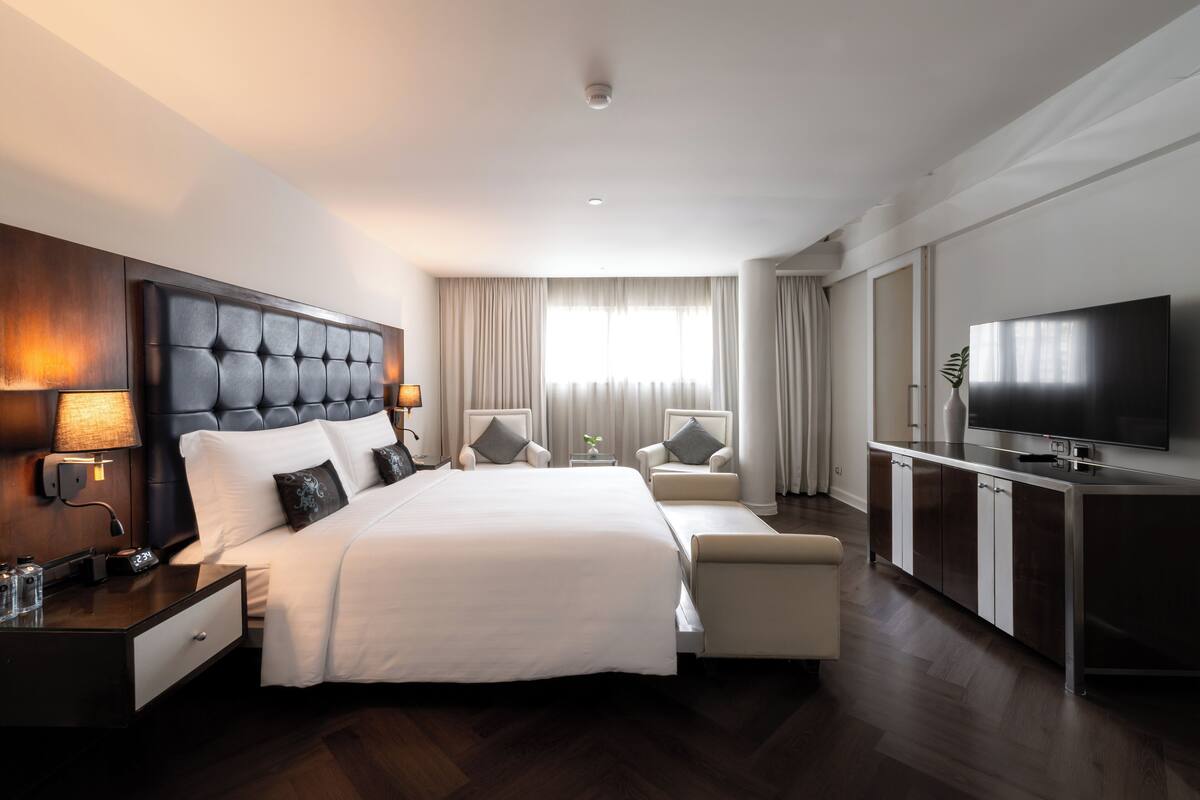 A modern hotel room with a large bed, a TV, a desk, and a seating area.