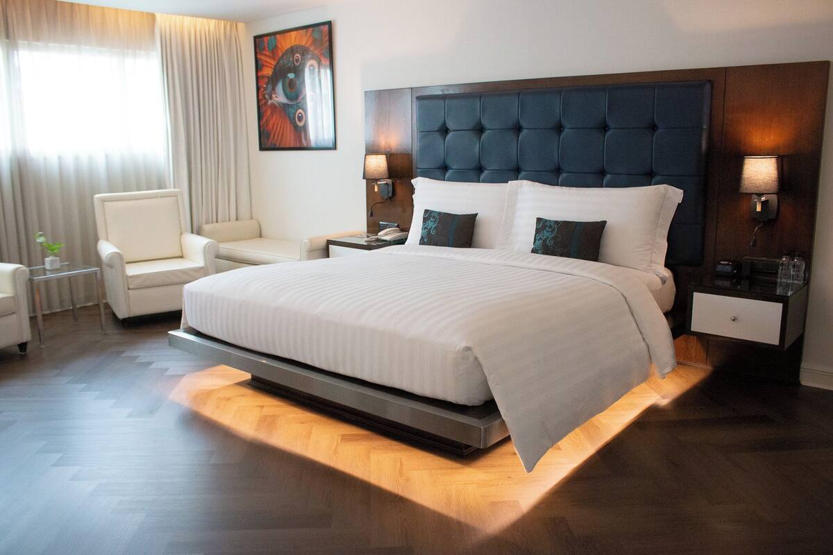 A modern hotel room with a large bed, a chair, a nightstand, and a lamp.