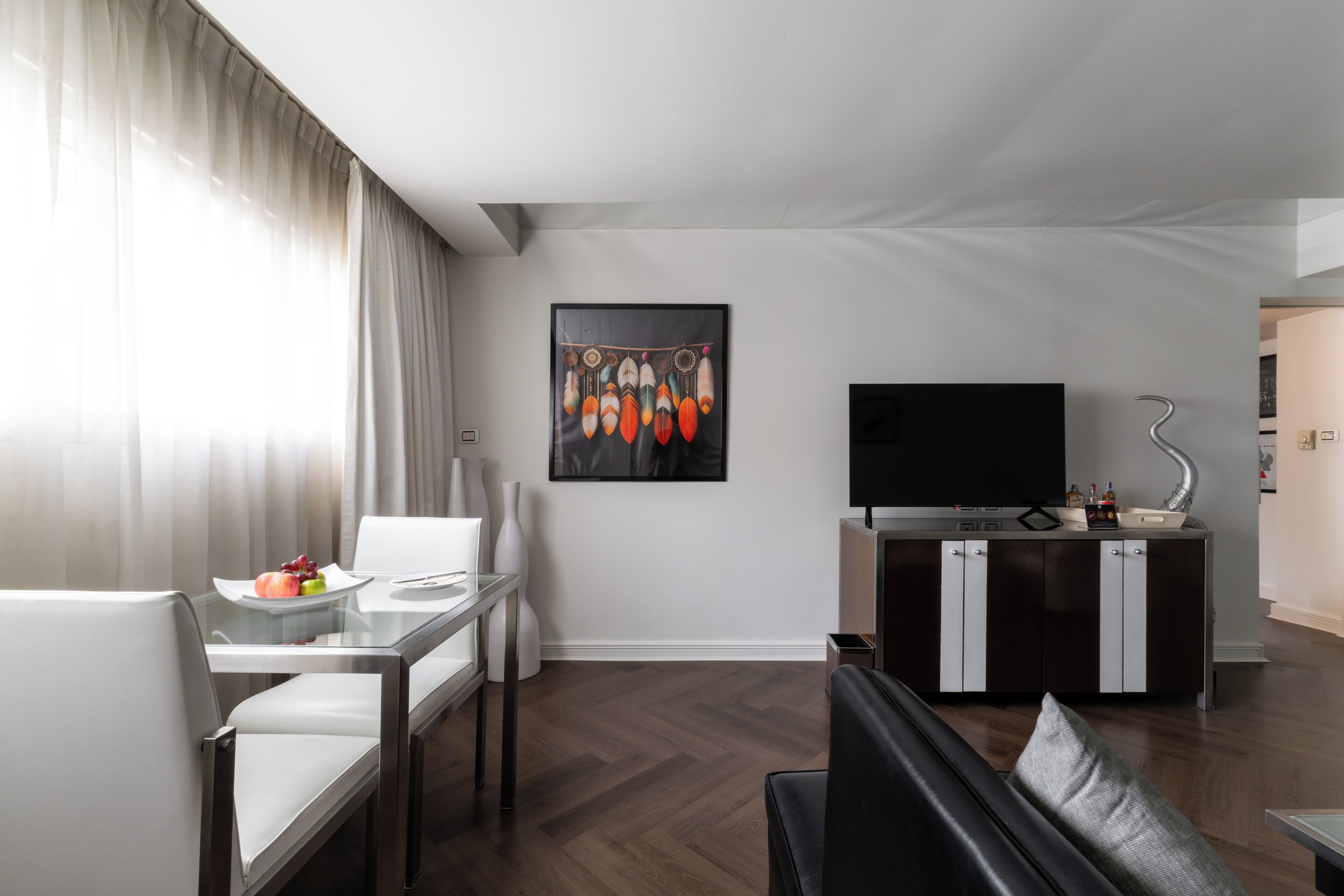 A modern living room with a dining area, a flat-screen TV, and a kitchen area with a sink and cabinets.