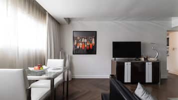 A modern living room with a dining area, a flat-screen TV, and a kitchen area with a sink and cabinets.