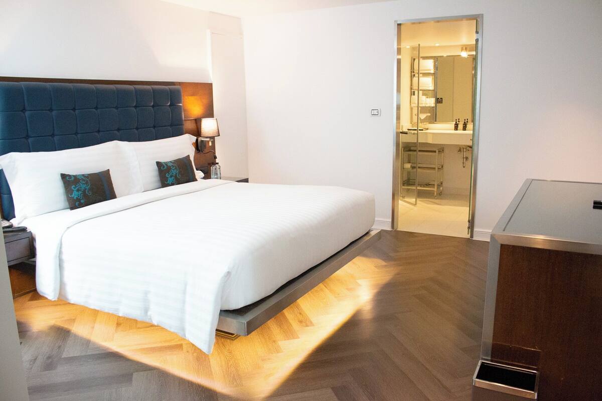 A modern hotel room with a large bed, a bedside table with a lamp, and a view into the bathroom.