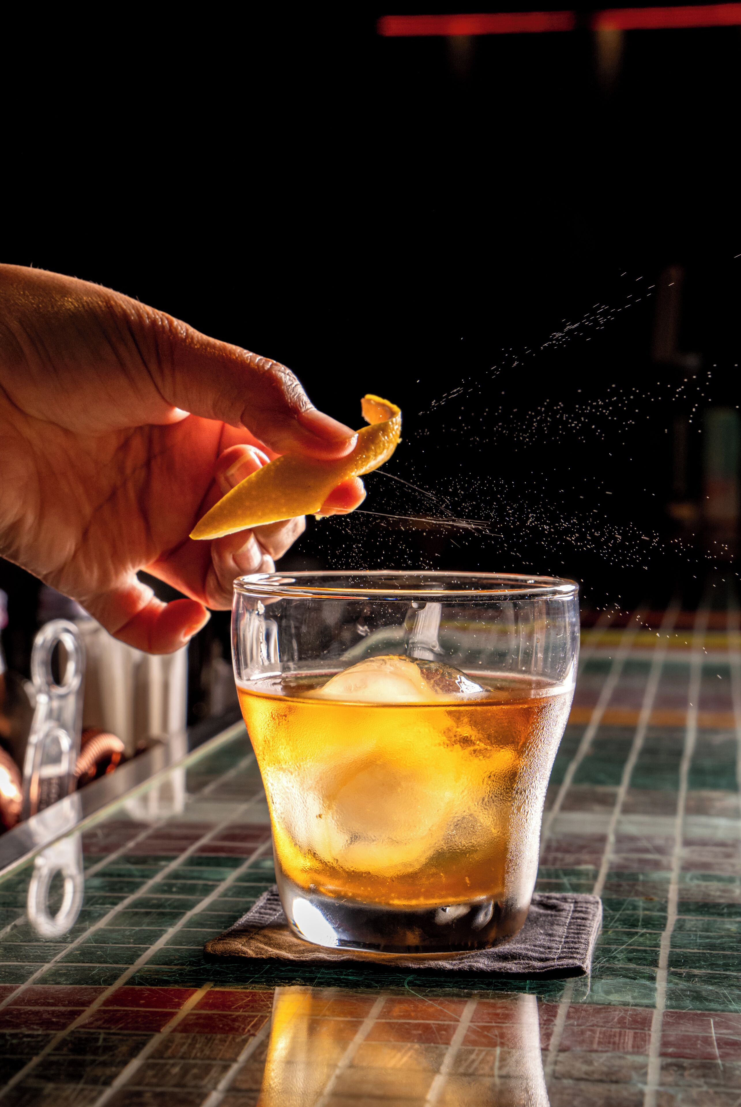 A hand sprinkling a substance into a glass with ice cubes.