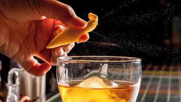 A hand sprinkling a substance into a glass with ice cubes.
