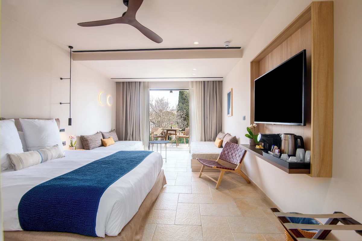 Habitación de hotel moderna con una cama grande, televisión de pantalla plana, ventilador de techo y vistas al exterior.