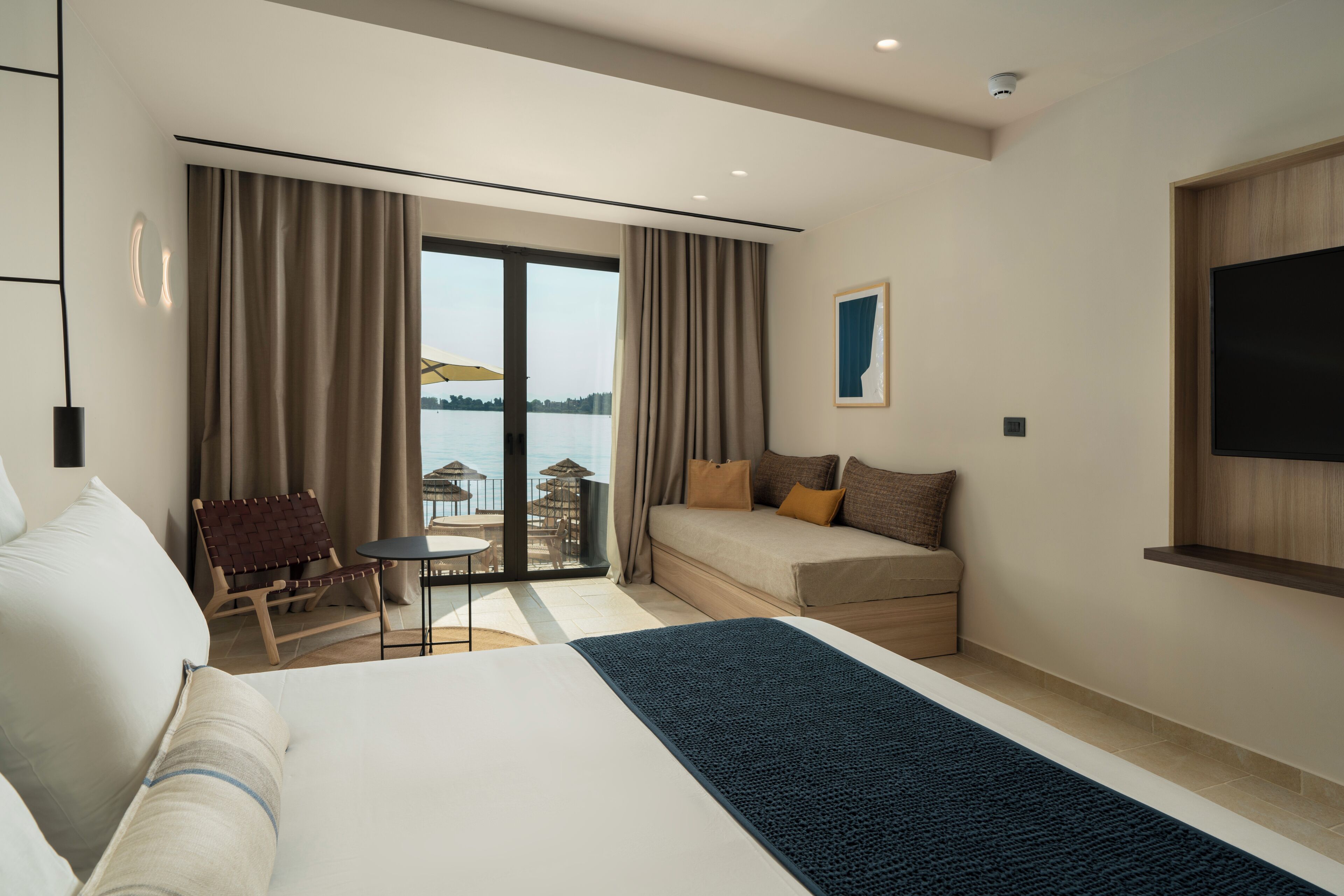 A hotel room with a large bed, a sofa, a chair, a small table, and a view of the sea.
