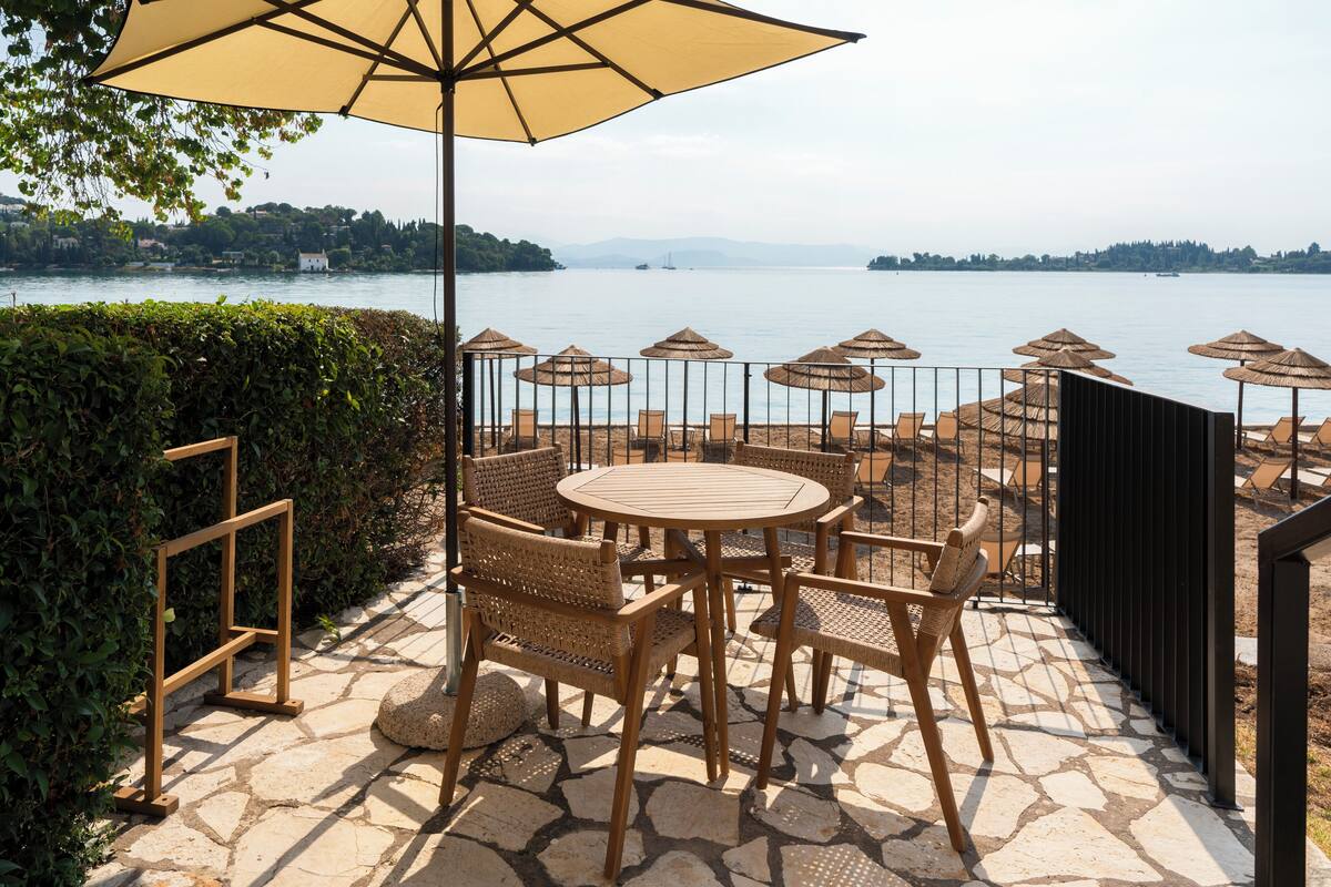 Una terraza con mobiliario de mimbre, piso de piedra y vista a un lago.