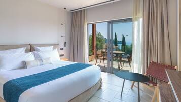 Habitación de hotel con una cama grande, un balcón con mesa y sillas, y vistas al mar.