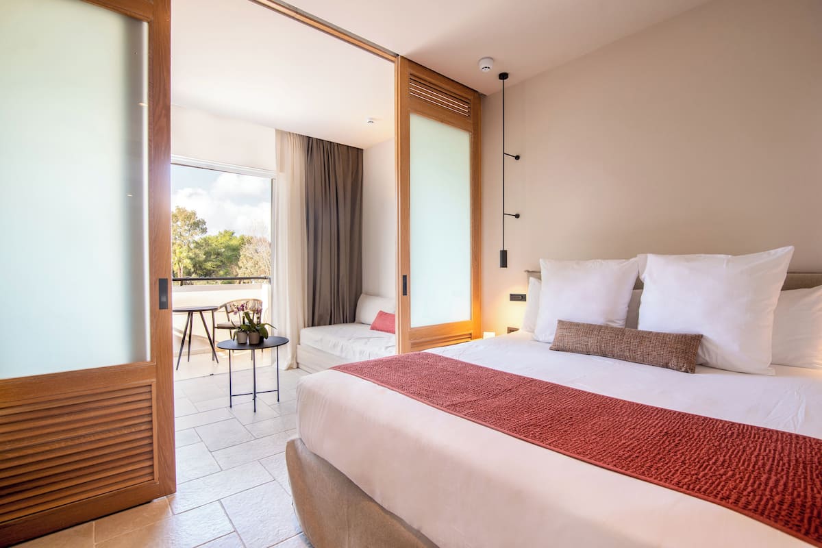 Habitación de hotel con una cama grande, una mesita con una silla y vistas al exterior.
