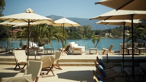 Un espace aménagé au bord de la piscine, avec des chaises longues et des parasols, offrant une vue sur un plan d’eau et des montagnes.
