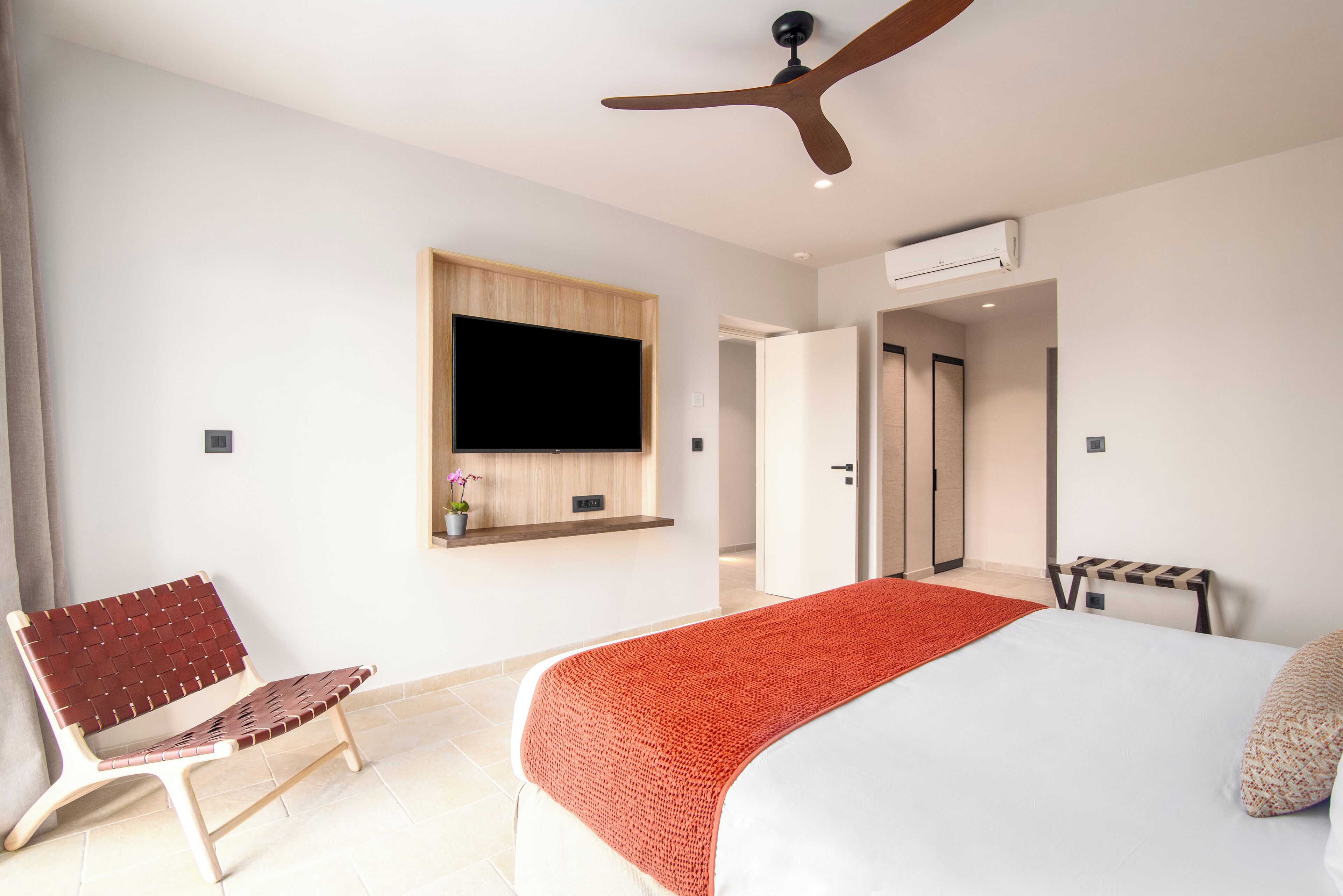 A modern hotel room with a bed, a bench, a TV mounted on the wall, and a ceiling fan.
