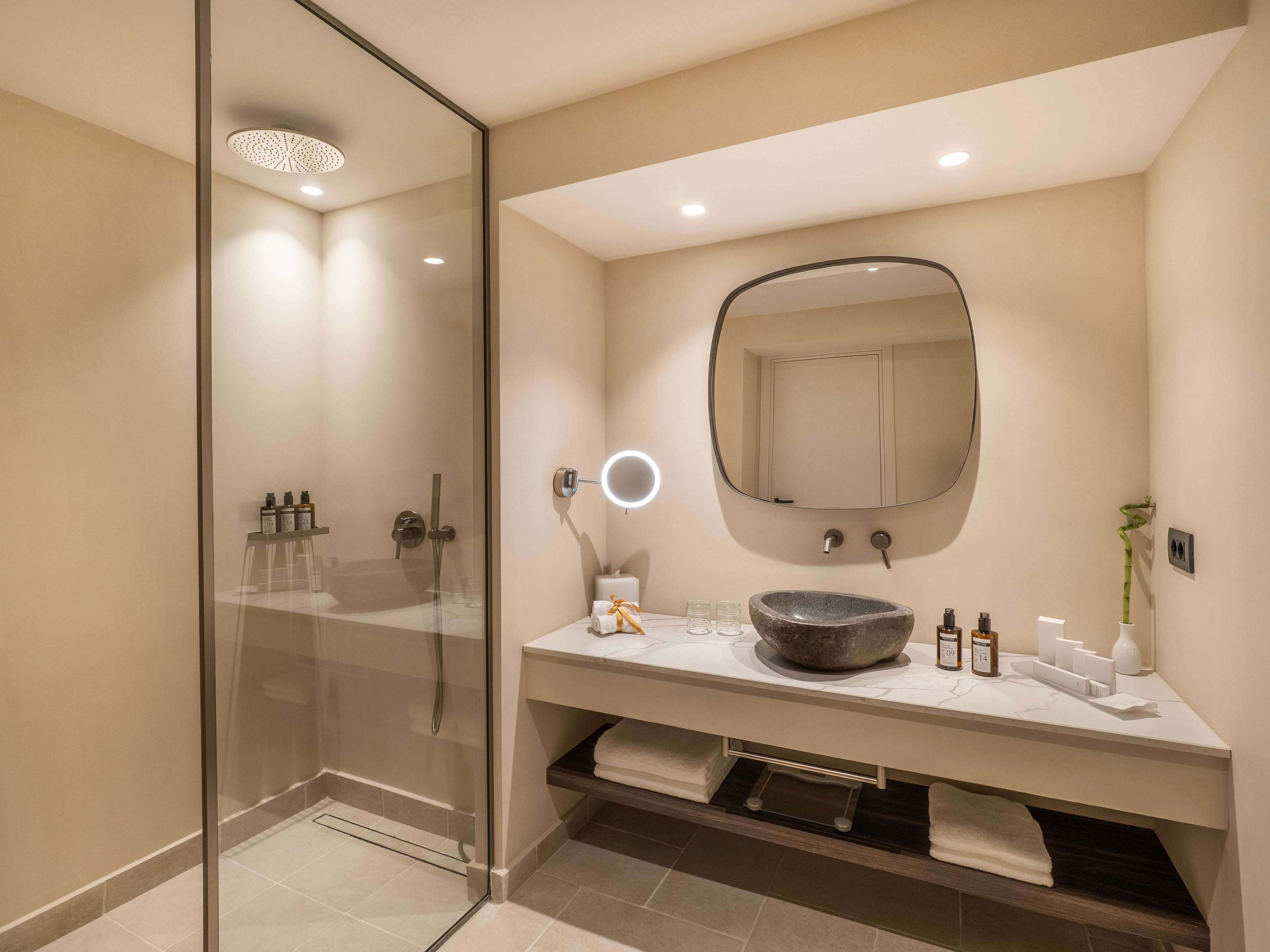 Une salle de bain moderne dotée d’une douche à parois de verre, d’un lavabo en marbre, d’un grand miroir et d’une commode avec un porte-serviettes.