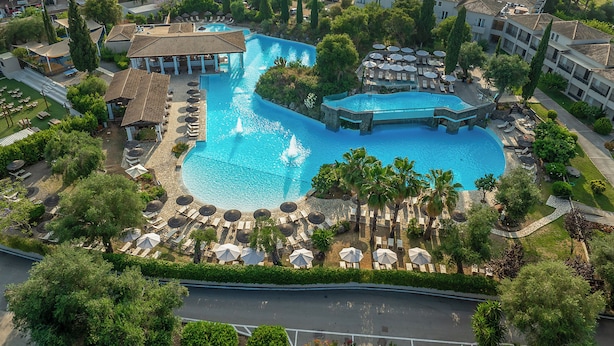 Vue aérienne d’un complexe hôtelier doté d’une grande piscine, de chaises longues et d’un espace abrité avec des parasols.