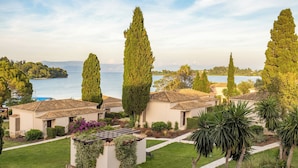 Une villa côtière avec un toit en tuiles de terre cuite, entourée d’une végétation luxuriante et de grands cyprès.