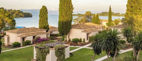 A coastal villa with a terracotta roof, surrounded by lush greenery and tall cypress trees.