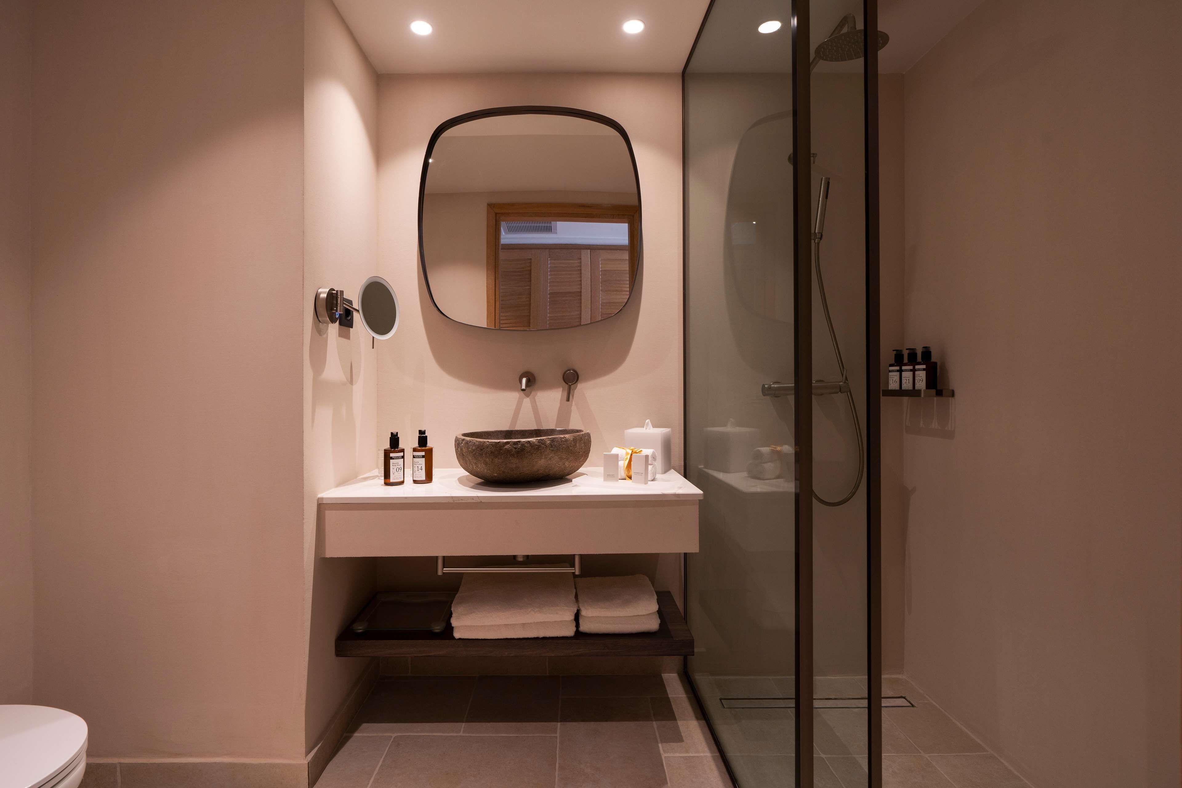 Un bagno moderno con un ampio specchio, un lavabo in pietra e una cabina doccia in vetro.
