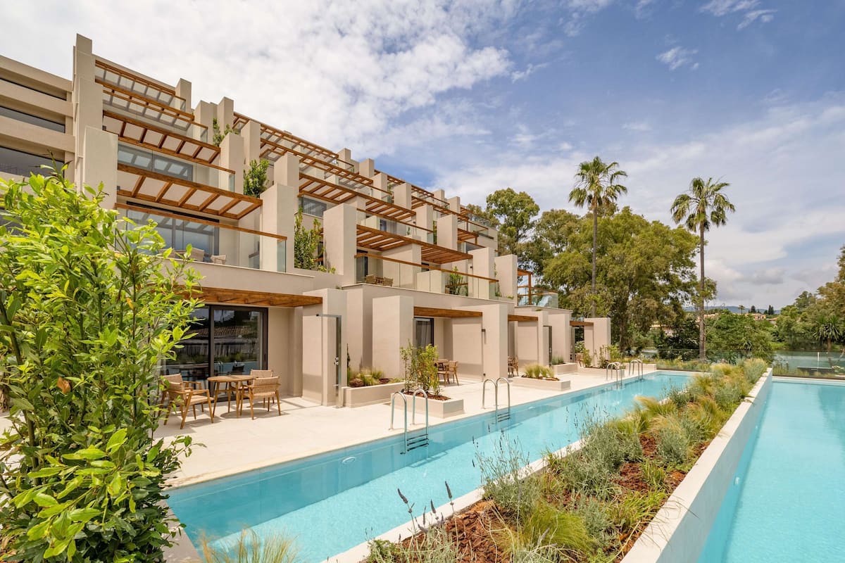 Un hotel moderno con piscina, mobiliario exterior y exuberante vegetación.
