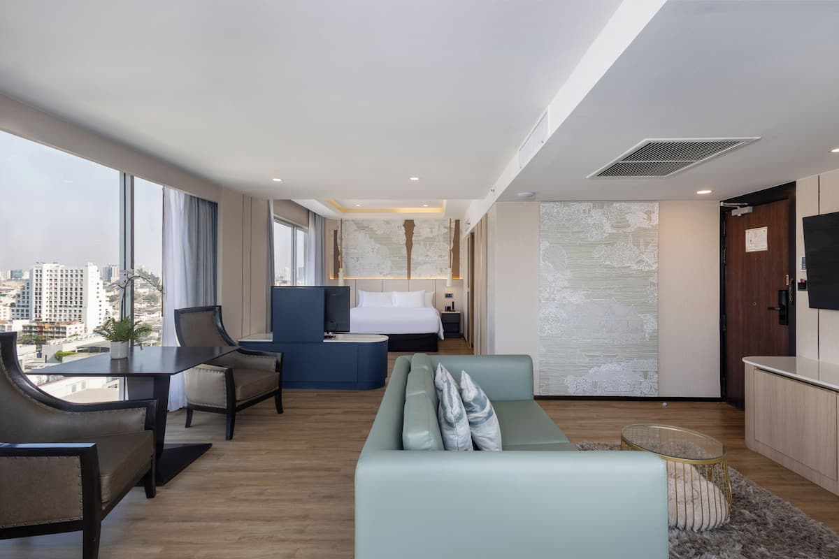 A modern hotel room with a bed, seating area, desk, and city view.