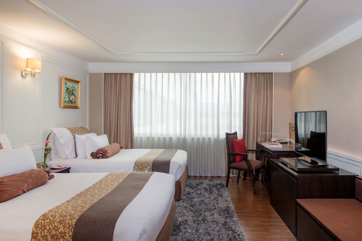 A hotel room with two beds, a desk, a television, and a large window with curtains.