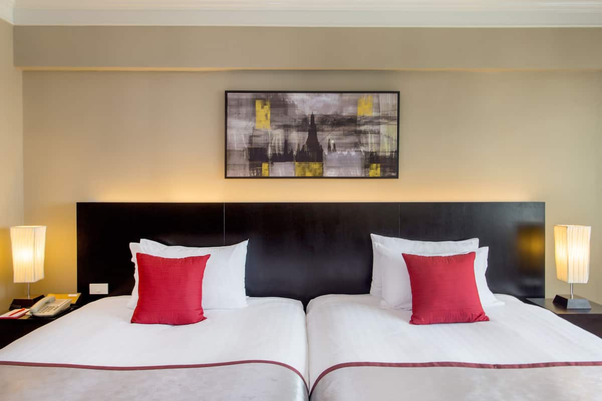 A hotel room with two beds, a large abstract painting on the wall, and bedside lamps.
