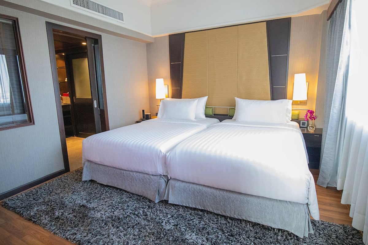A double bed with white linens, a dark headboard, two bedside lamps, and a grey shaggy rug.