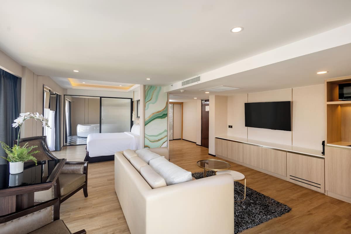 A modern hotel room with a sofa, a dining table, a TV, and a bed.