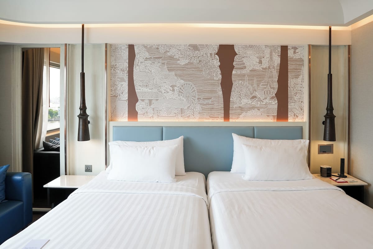 A hotel room with two beds, a desk, a chair, and a large decorative wall.