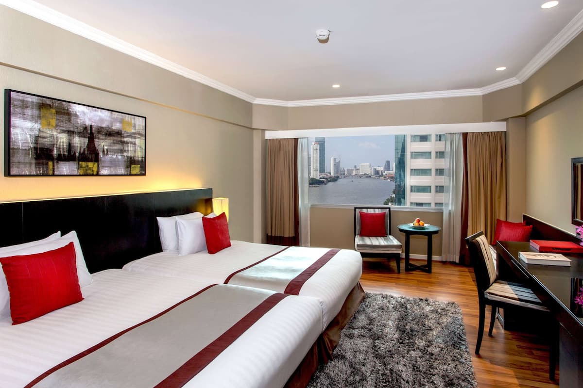 A hotel room with two beds, a desk, and a view of a cityscape.