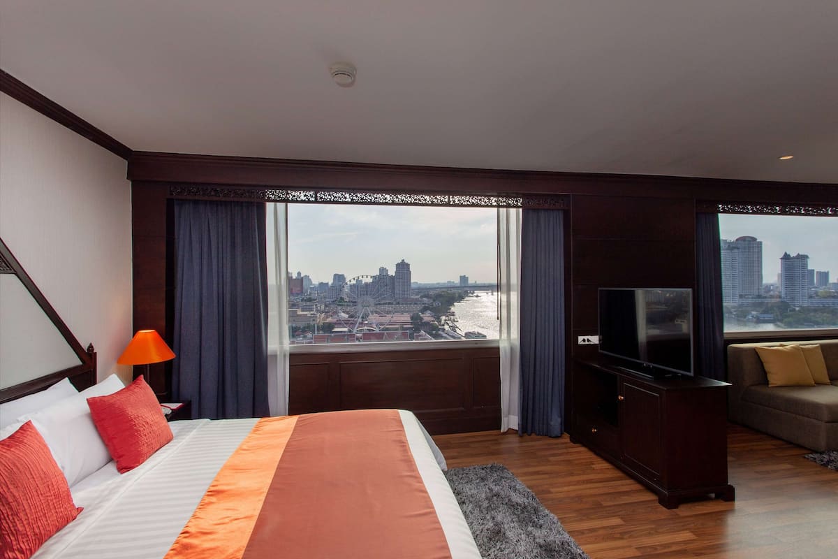 A hotel room with a large bed, a TV, a sofa, and a view of a cityscape and river.