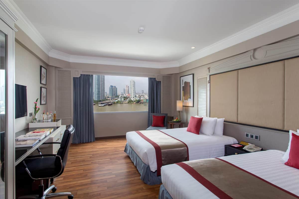 A hotel room with two beds, a desk, and a view of a cityscape.