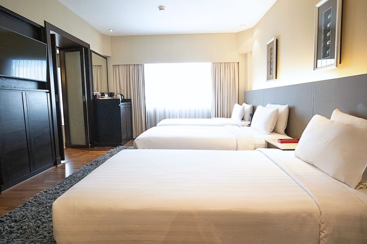 A hotel room with two beds, a desk, a wardrobe, and a large window with curtains.