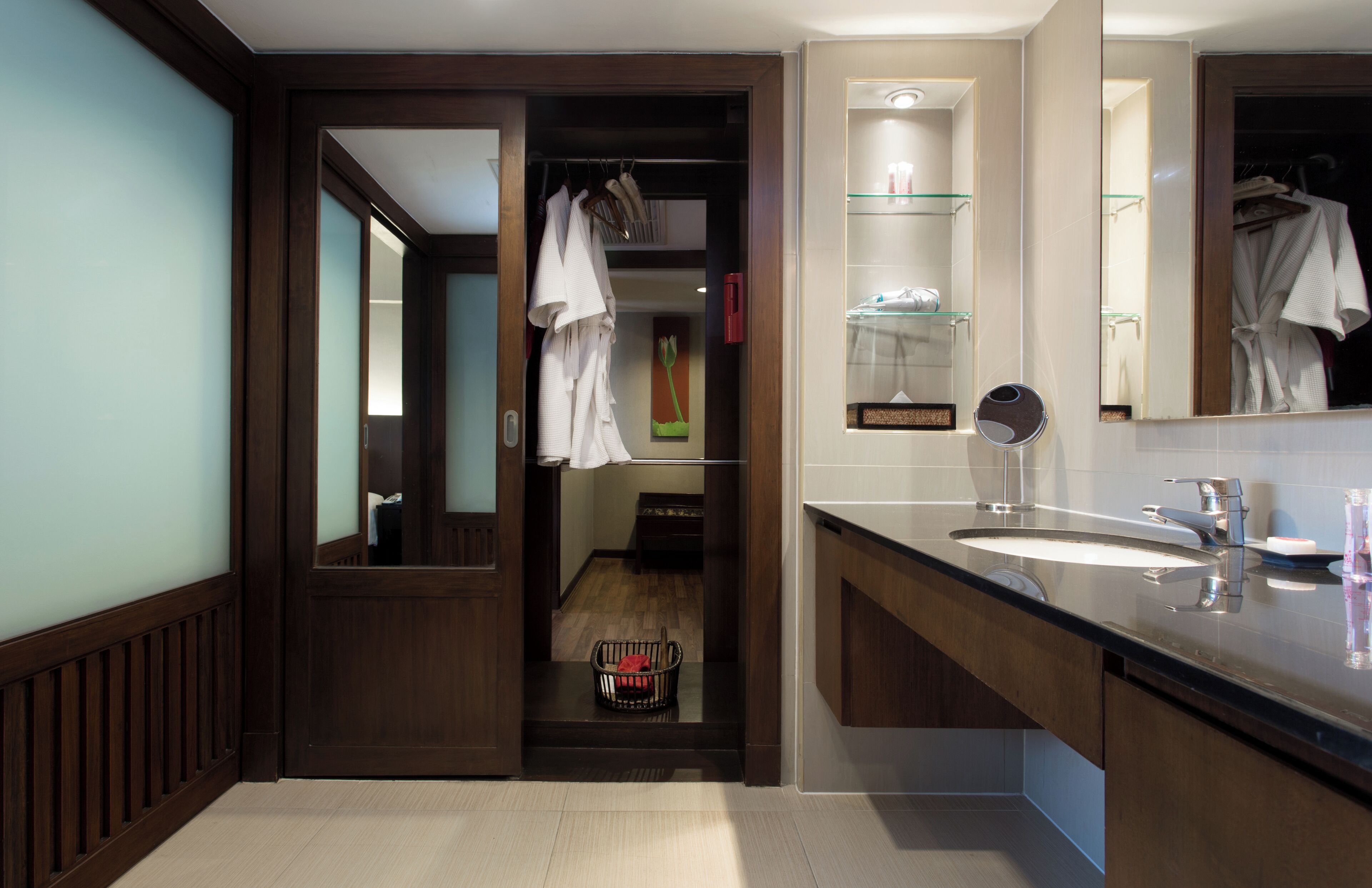 A modern bathroom with a wooden vanity, a large mirror, and a walk-in closet with hanging clothes.