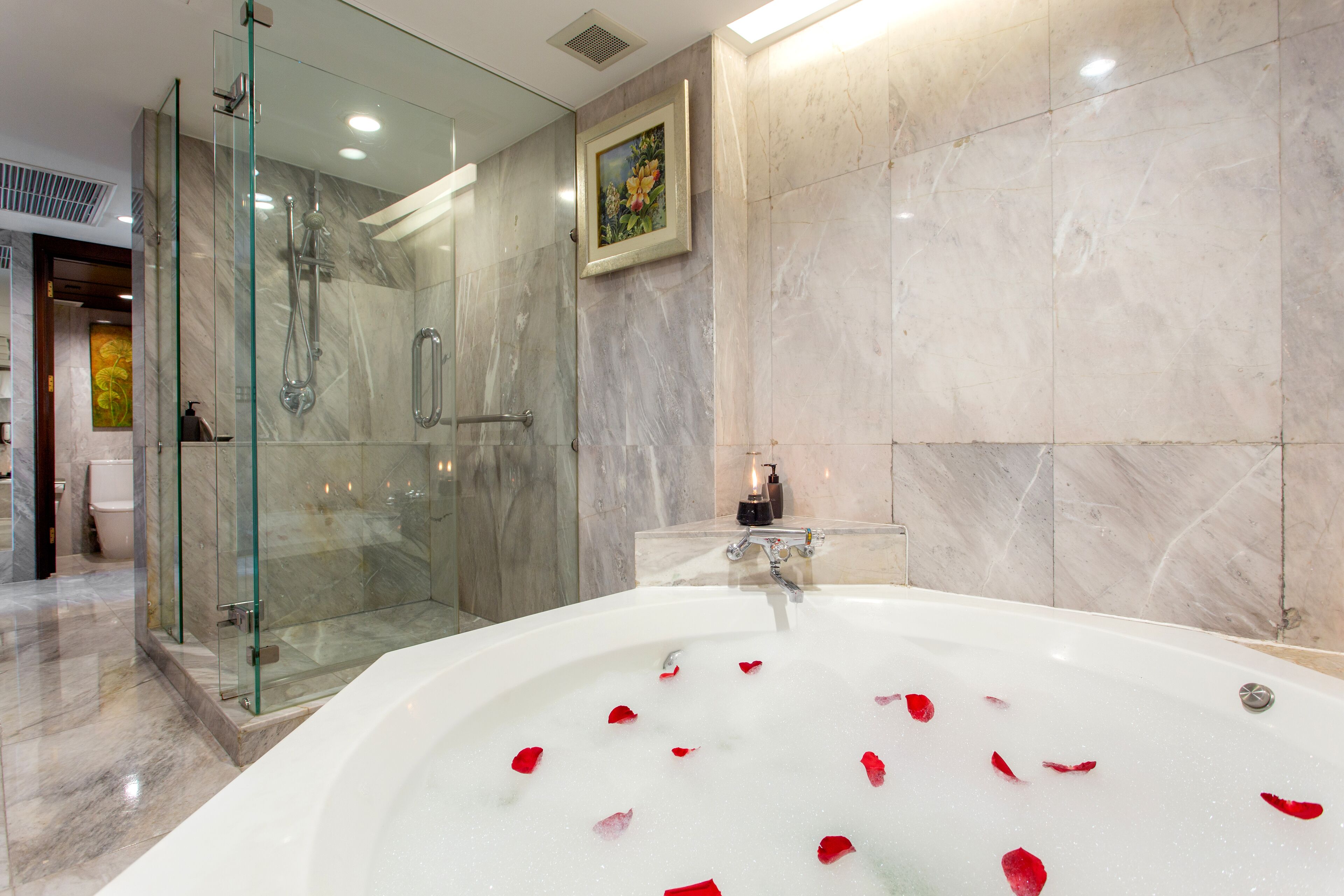 Un baño moderno con ducha envuelta en vidrio, una bañera grande con pétalos de rosa y paredes de mármol.