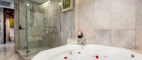 Un baño moderno con ducha envuelta en vidrio, una bañera grande con pétalos de rosa y paredes de mármol.
