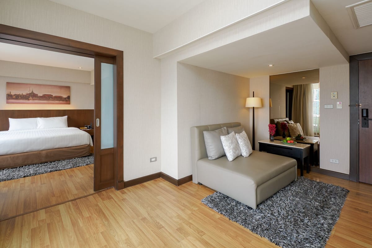 A hotel room with a bed, a sofa, a desk with a lamp, and a mirror.