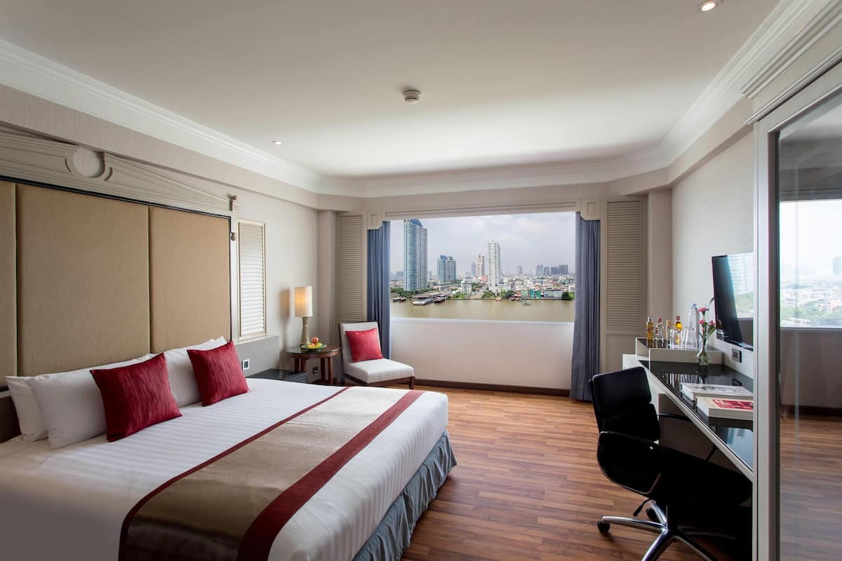 A hotel room with a large bed, a desk, and a view of a cityscape and water.