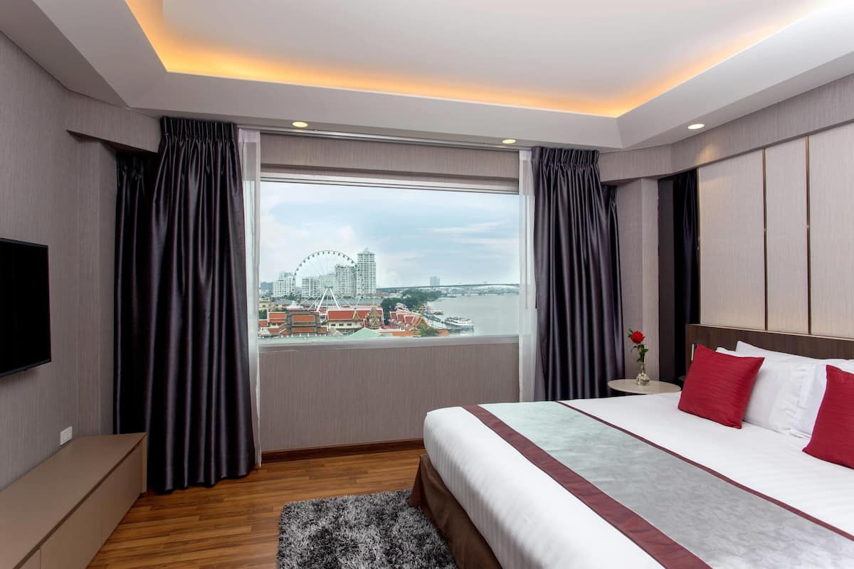 A hotel room with a large bed, a TV, a window with curtains, and a view of a cityscape.