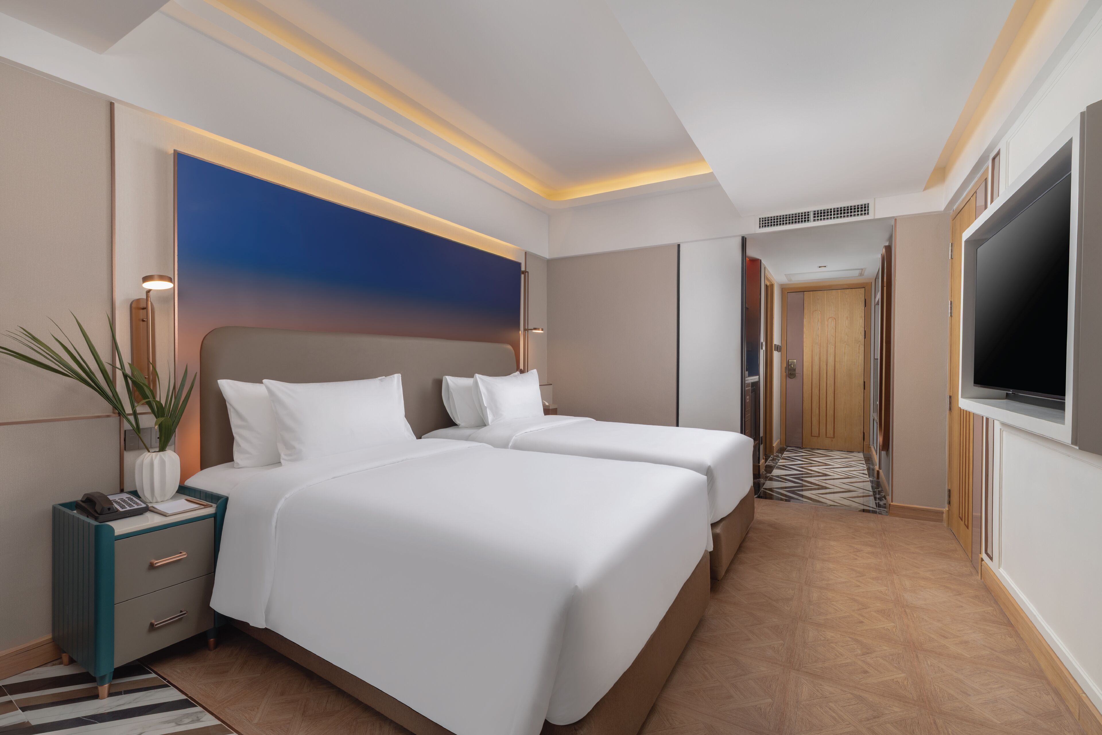 Ein Hotelzimmer mit zwei Betten, einem großen Fernseher, einem Schreibtisch mit Lampe und Blick auf den Flur.