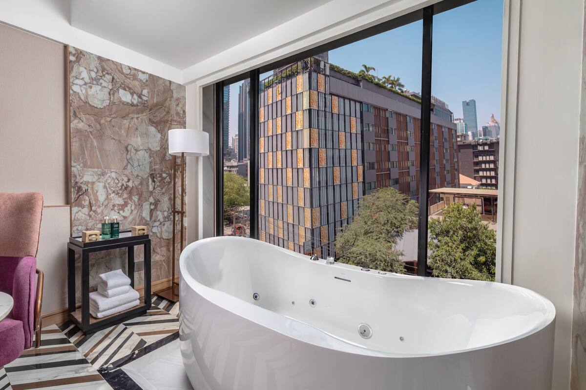 A modern bathroom with a freestanding bathtub, a marble wall, and a large window offering a city view.