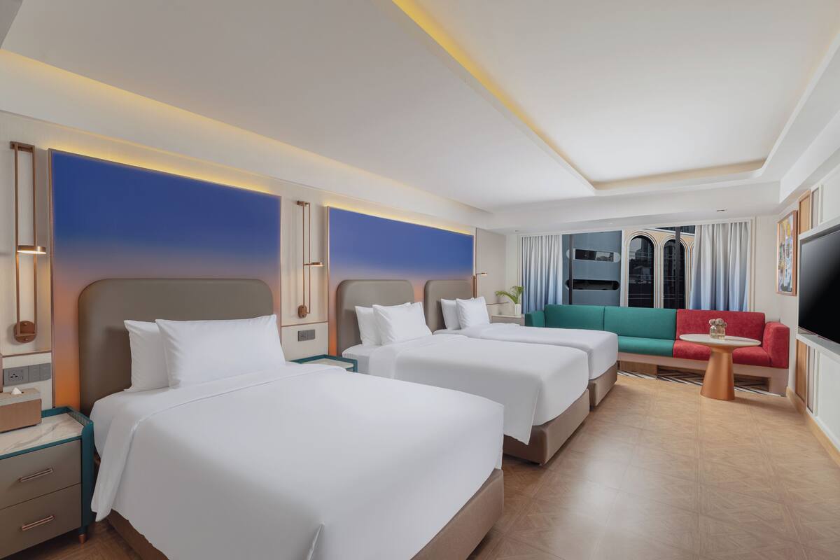 A hotel room with two beds, a sofa, a TV, and a window with curtains.